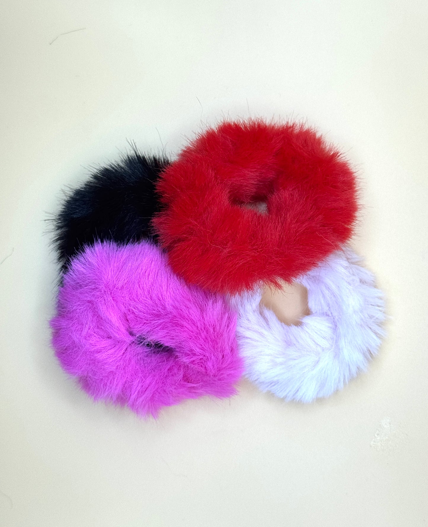 Four colorful fluffy scrunchies on a light background