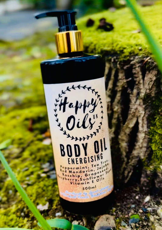 A bottle of Happy Oils UK Body Oil Energising, 500ml, featuring a black pump and gold collar, set against a mossy tree stump background.