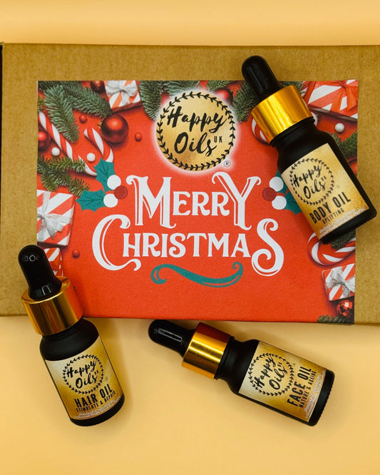 Three 10ml mini bottles of 'Happy Oils UK' hair oil face oil and body oil with a decorative Christmas box in the background.