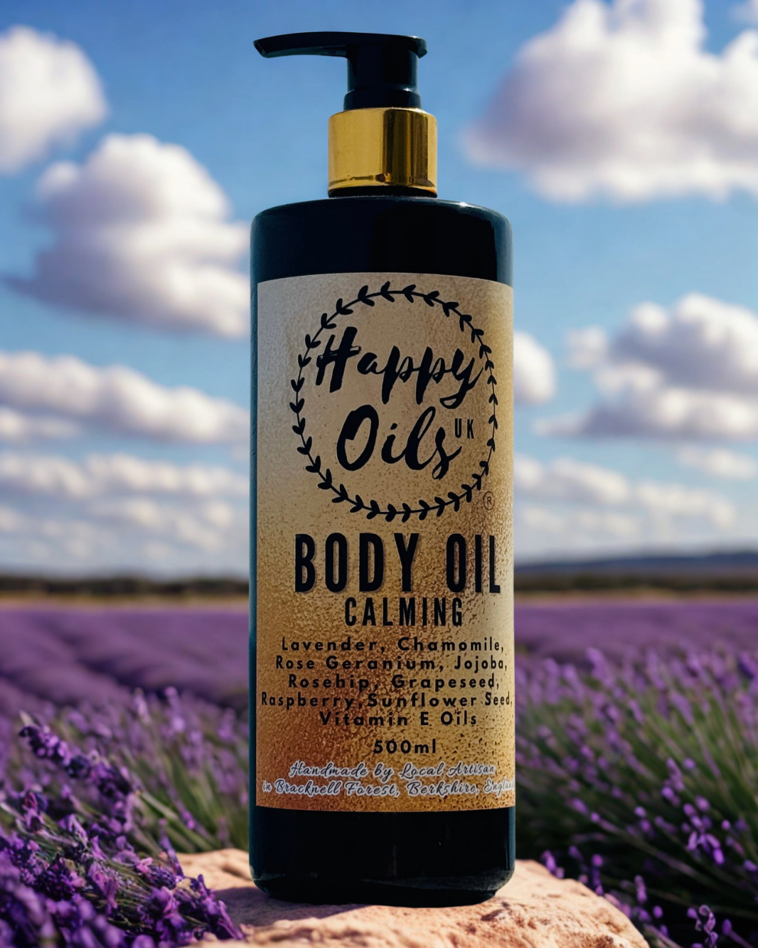 A 500ml pump bottle of Happy Oils UK Body Oil, Calming, placed on a rock in a lavender field under a blue sky with clouds. The bottle is black with a gold collar and a beige label.
