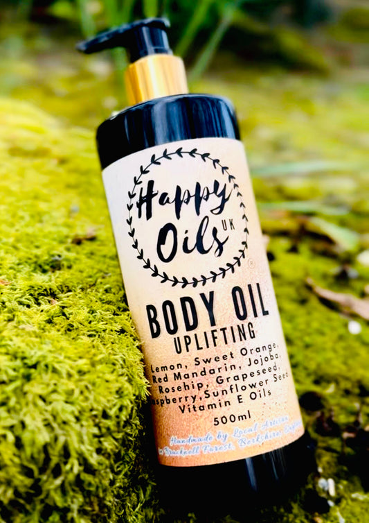 Happy Oils UK Uplifting Body Oil 500ml pump bottle resting on green moss — red mandarin, lemon and sweet orange with nourishing jojoba and rosehip